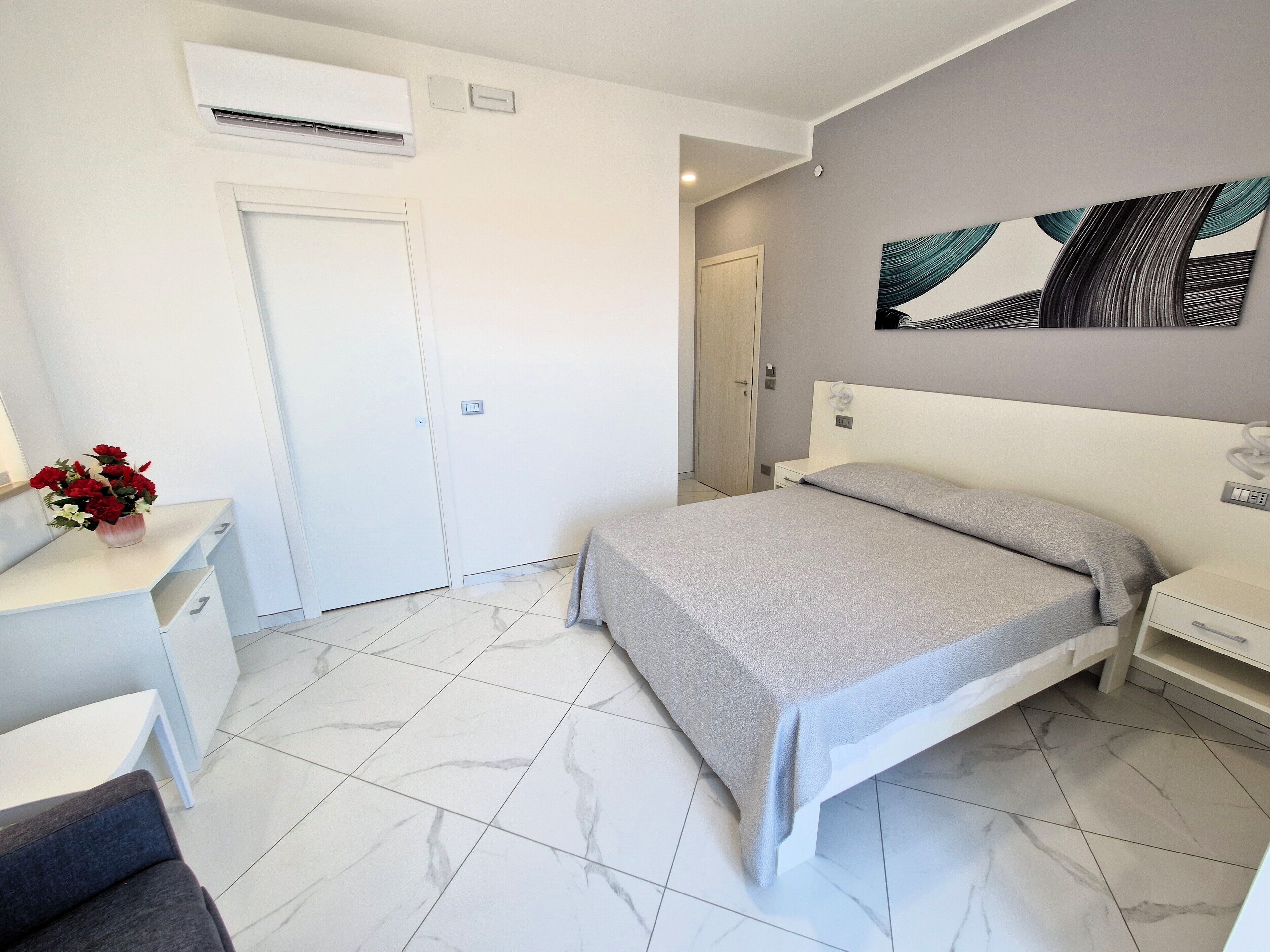 A modern bedroom with a bed, bedside table, and a desk with a vase of flowers.