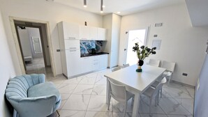 A modern kitchen with white cabinets and a marble backsplash, a dining area with a white table and chairs, and a light blue sofa. - Al 211 Rooms (Pizzo)