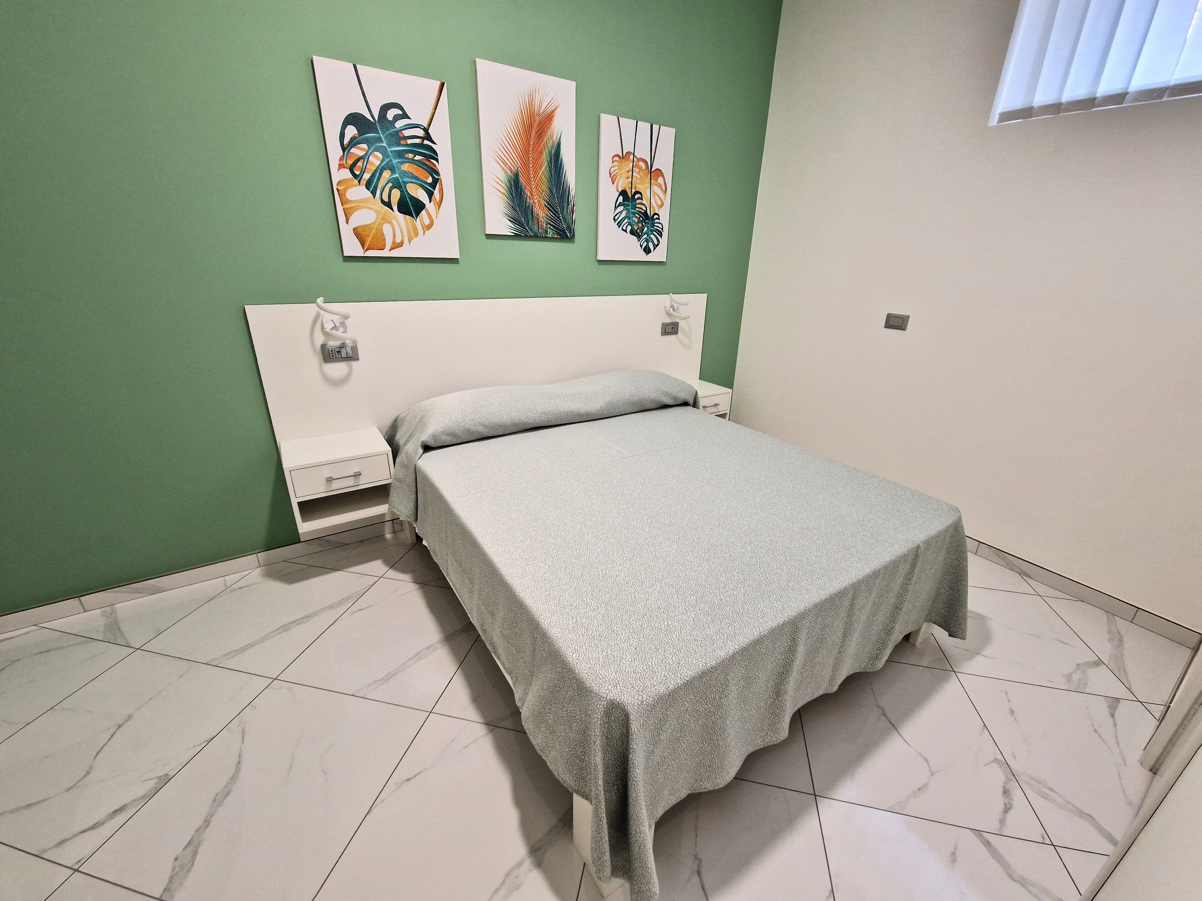 A bedroom with a bed, green walls, and artwork on the wall.