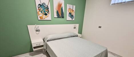 A bedroom with a bed, green walls, and artwork on the wall.