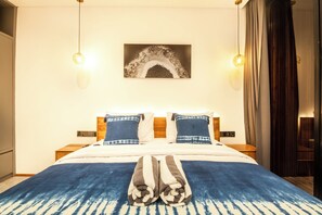 Una cama bien hecha con una manta azul y blanca, dos almohadas y un par de toallas dobladas sobre la cama.