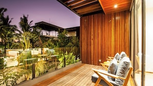 A wooden deck with a glass balustrade overlooking a garden, a seating area with cushions, and a wooden ceiling. - Coastal Haven: Fresh 4BR Villa 200m to Canggu (Canggu)
