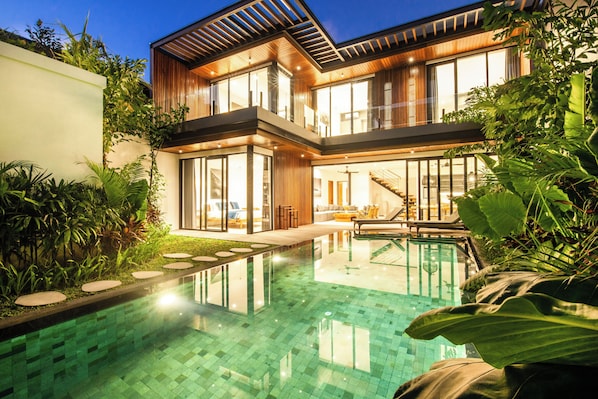 A modern two-story house with a swimming pool, large windows, and a well-maintained garden.
