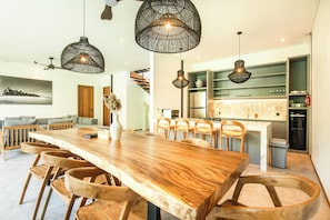 A modern kitchen with a central island, wooden chairs, and hanging pendant lights.