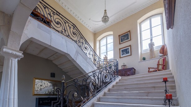 Una gran escalera con barandillas negras ornamentales, un candelabro y una estatua.