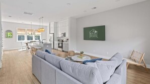 A spacious living room with a grey sofa, a dining area with wooden furniture, and a kitchen in the background.