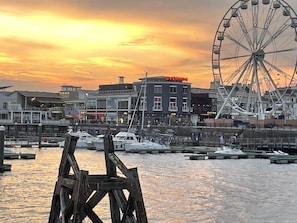 A waterfront marina with boats docked, a Ferris wheel, and buildings with signage.