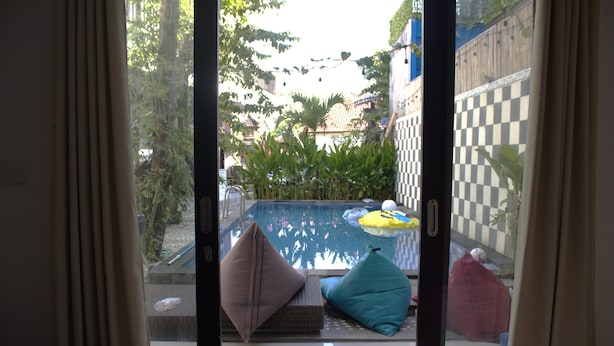 Vista a través de un ventanal de un área de piscina con cojines y una pared a cuadros.