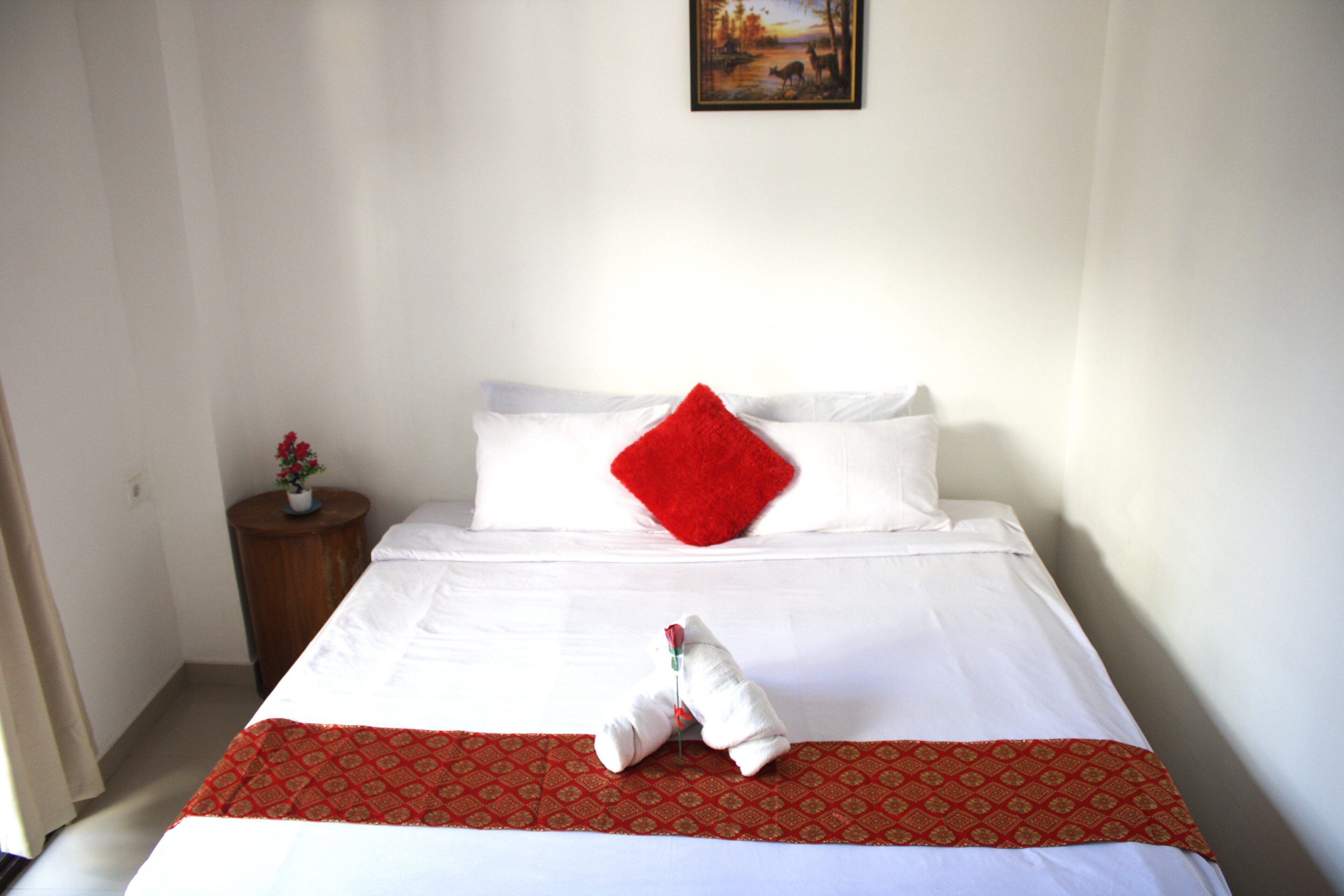 A neatly made bed with a red pillow, a white pillow, and a red and white patterned bedspread.