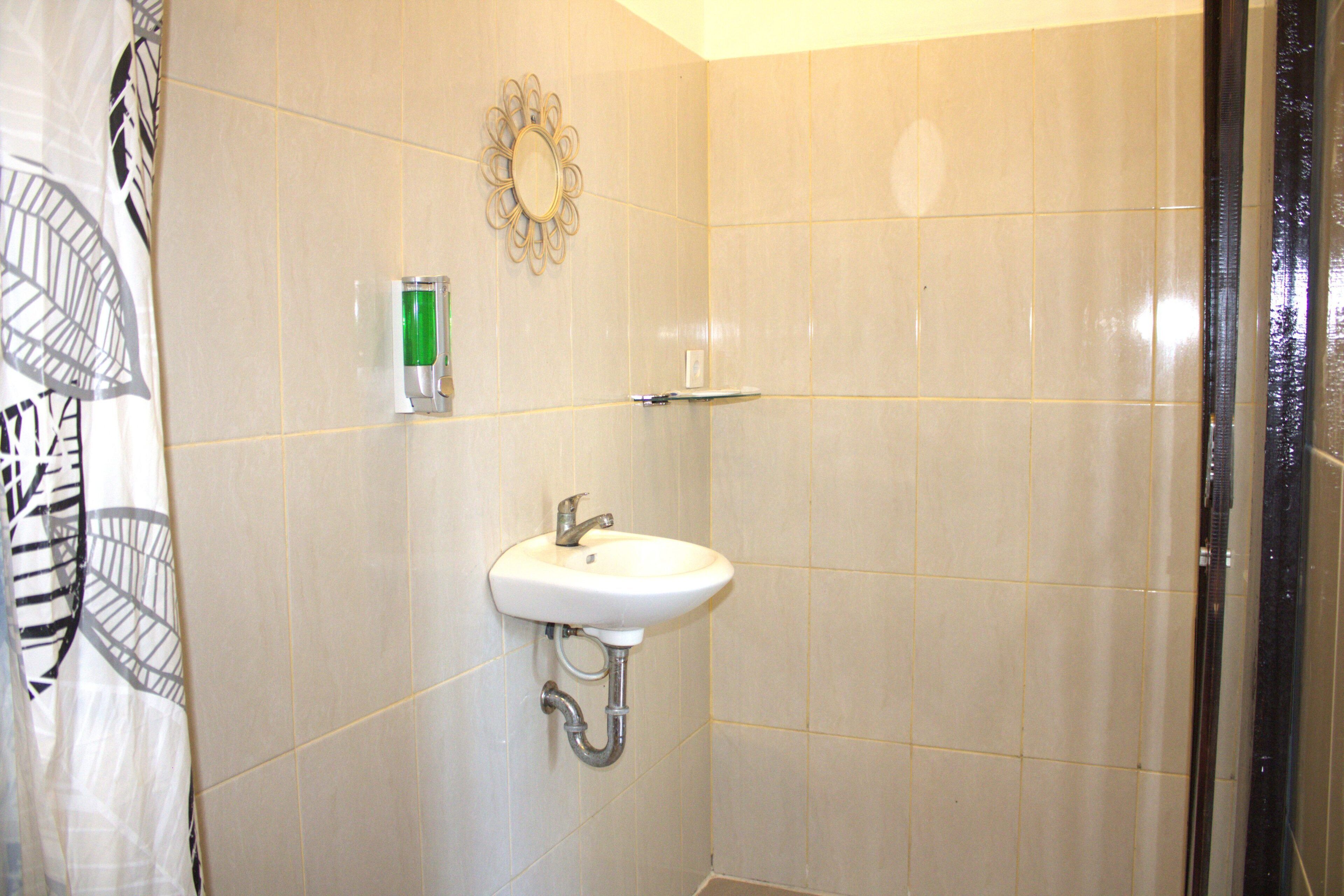 Un baño con lavamanos blanco, espejo y zona de ducha.