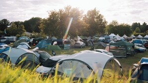A campsite with multiple tents and vehicles, set in a grassy area with trees in the background. - Bronze Camping (Le Mans)