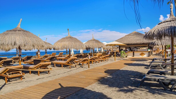 A beach with wooden lounge chairs and thatched umbrellas, a wooden walkway, and a beach bar. - SeaShell Crown Luxury Suite (Costa Adeje)