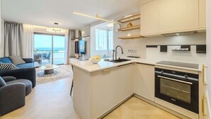 A modern kitchen with a built-in oven, a dining area with a table and chairs, and a living room with a sofa and a TV. - SeaShell Crown Luxury Suite (Costa Adeje)