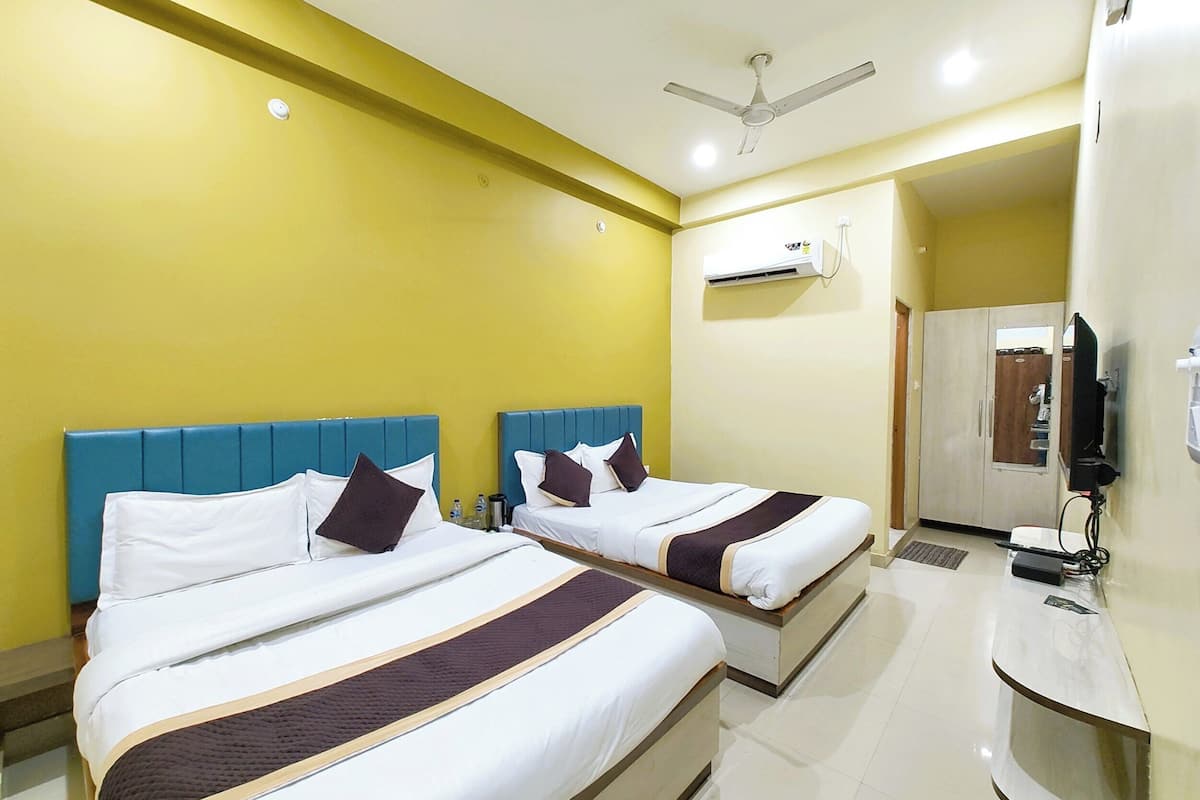 Habitación de hotel con dos camas, ventilador de techo, unidad de aire acondicionado, televisor y escritorio.