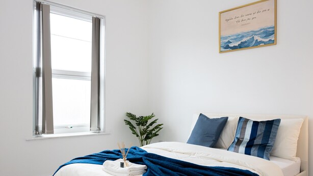 Ein Schlafzimmer mit Bett, Fenster, Wandbild und Zimmerpflanze.