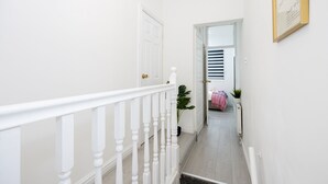 Eine Treppe mit weißen Geländern führt zu einem Raum mit einem Bett und einem Fenster mit Jalousien.