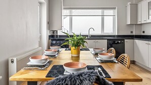 A modern kitchen with a dining area, featuring a wooden table, chairs, and a potted plant. - Spacious 4 Bedroom Townhouse Close to City Centre, Barbican, Hoe & Moors (Plymouth)