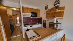 Una cocina compacta con armarios de madera, lavadora, microondas y un refrigerador pequeño.