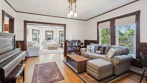 A spacious living room with a grand piano, a sectional sofa, a coffee table, and a bookshelf. - Historic Charm Meets Modern Luxury in Kennebunkport|Walk to Shops & Restaurants! (Kennebunkport)