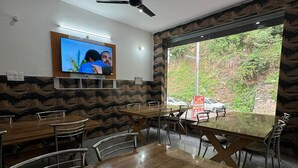 A dining area with wooden tables and metal chairs, a ceiling fan, and a television mounted on the wall. - Hotel Rest and Bite (Rajgarhi)