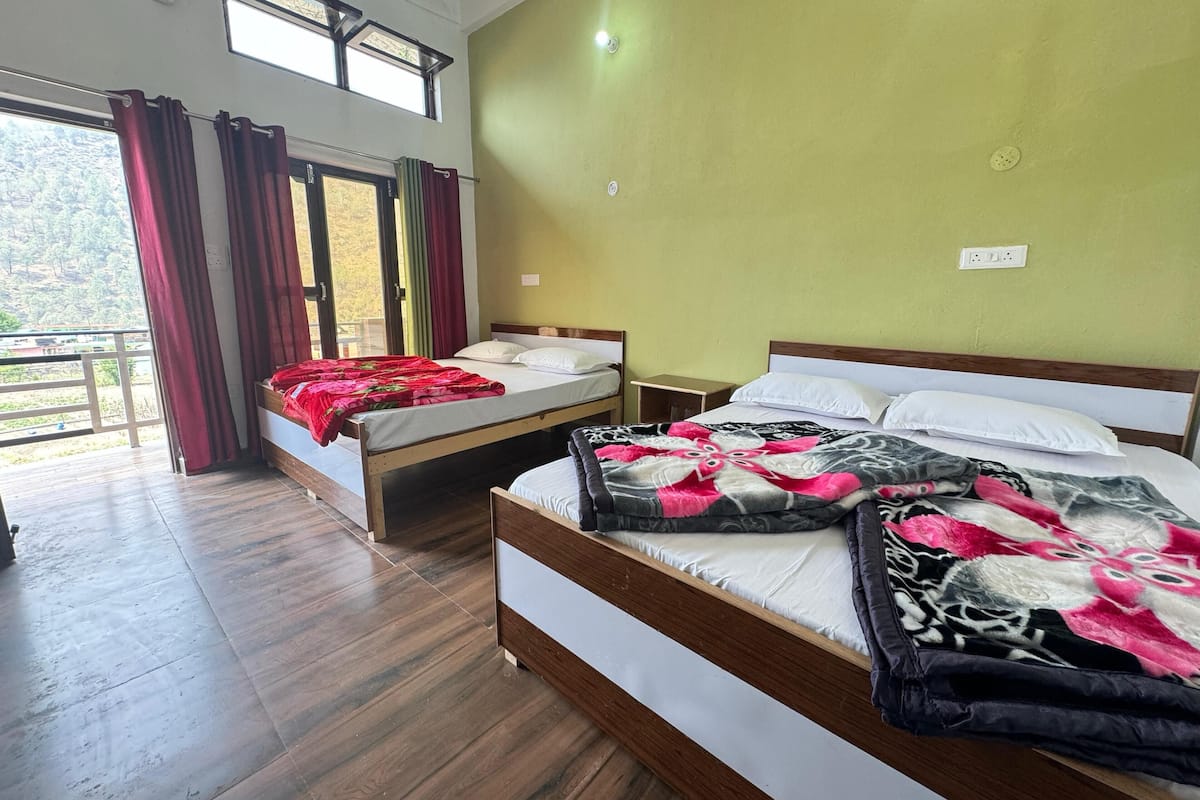 A room with two beds, wooden flooring, a balcony with curtains, and a view of the outdoors.