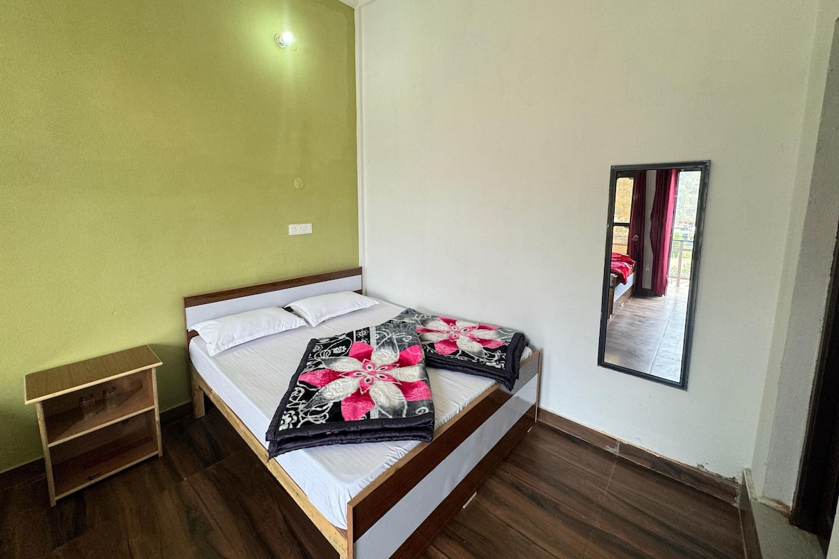 A single bed with a patterned blanket, a bedside table with glasses, and a mirror on the wall.