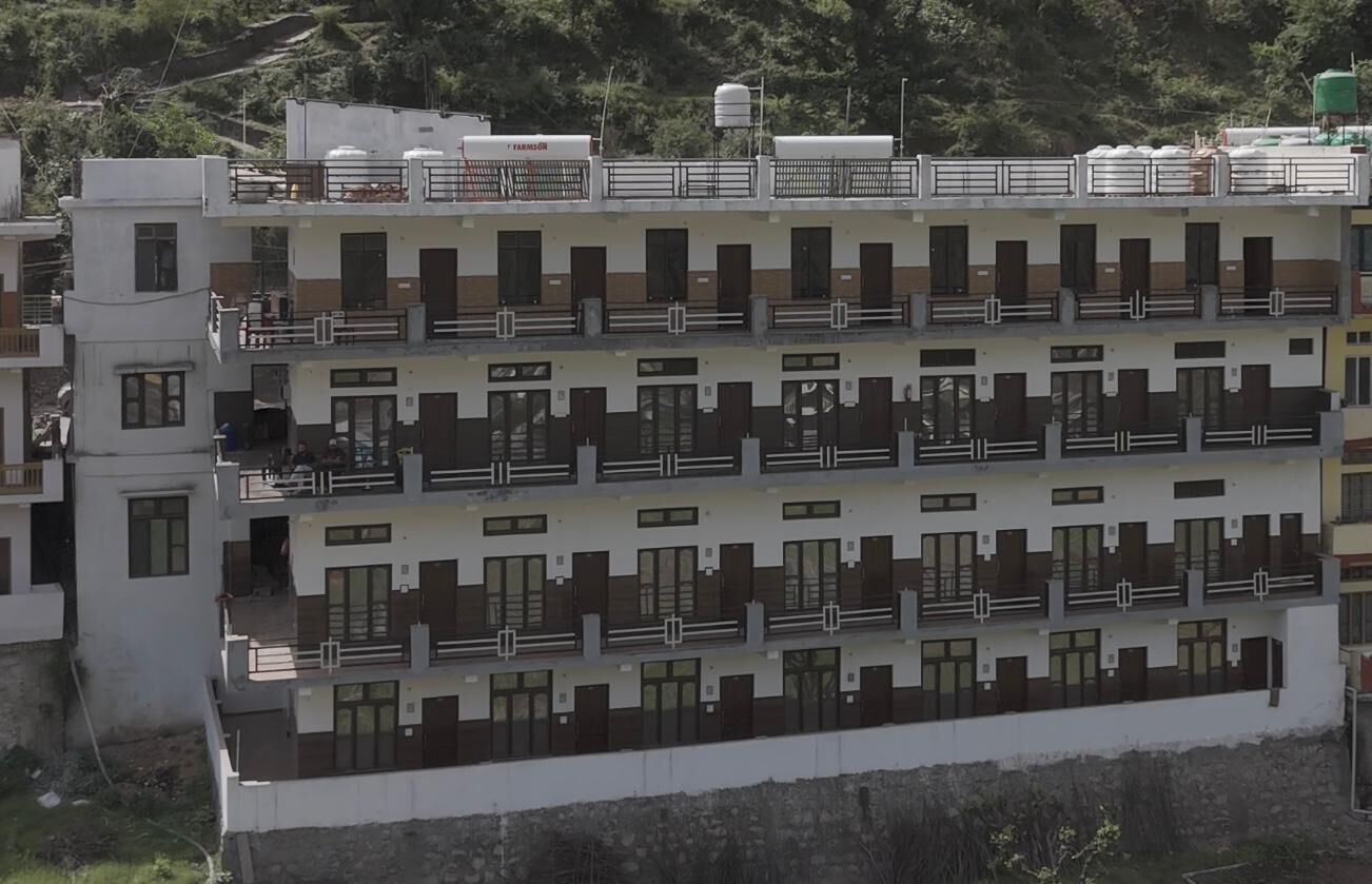 A multi-story residential building with balconies, a water tank on the roof, and a view of a hillside.