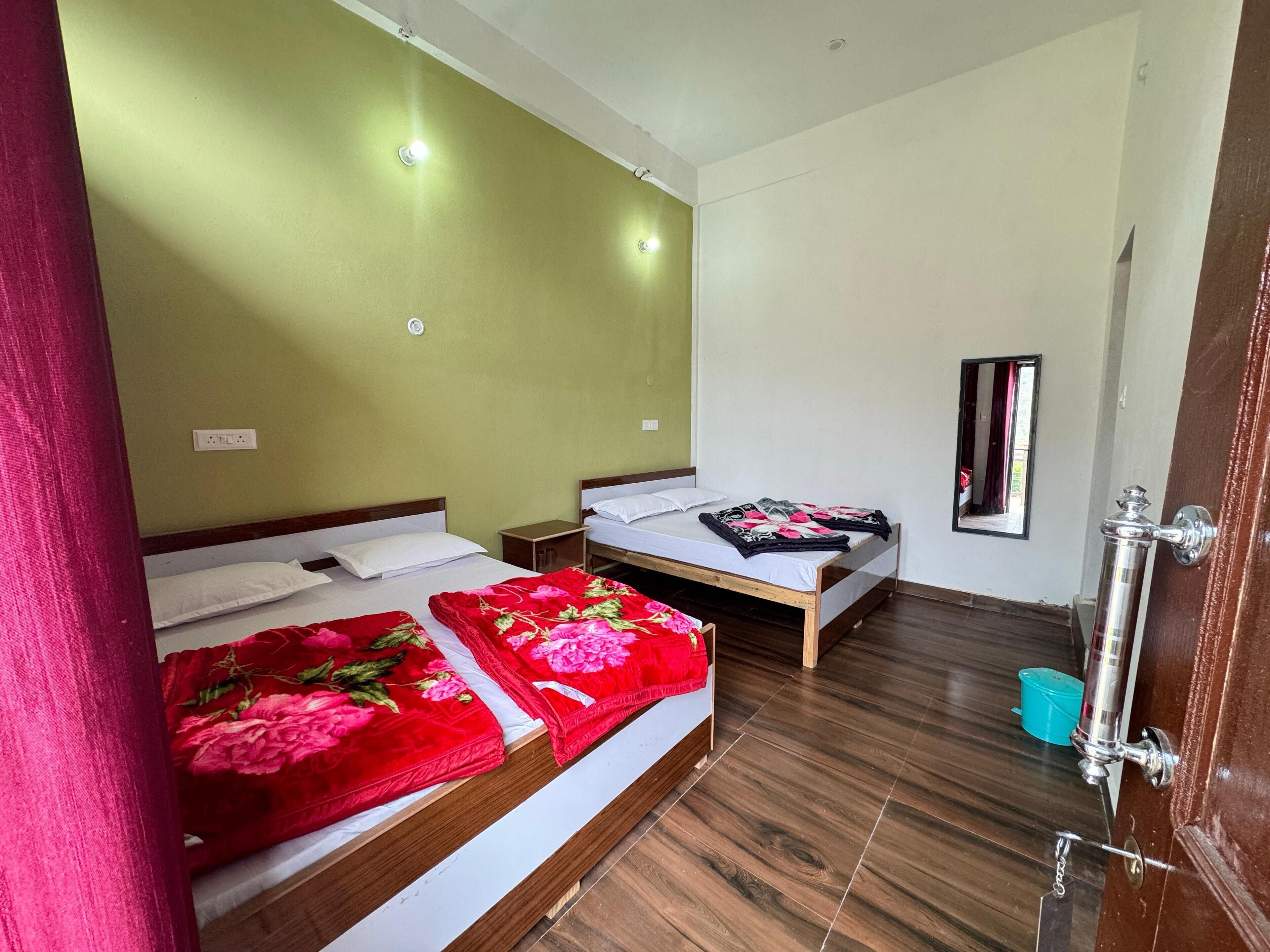 A hotel room with two beds, wooden flooring, a mirror, and a door with a handle.