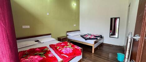 A hotel room with two beds, wooden flooring, a mirror, and a door with a handle.