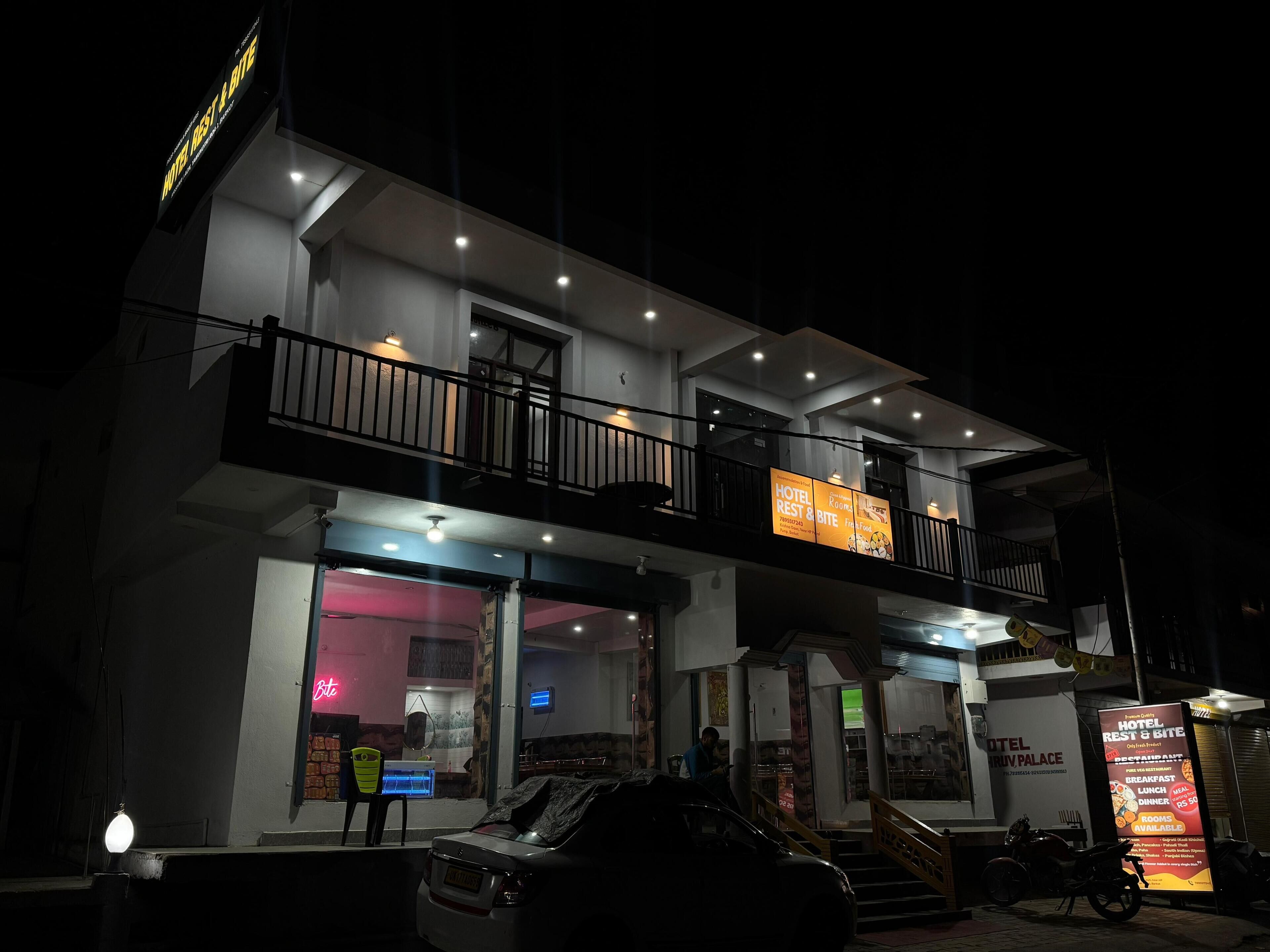 A two-story hotel with a balcony on the upper floor, a neon sign, and a signboard advertising hotel services.