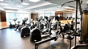 A gym with various exercise equipment, large windows, and a view of buildings outside. - Stylish 1BR Dubai Marina w Pool and Gym (Dubai)