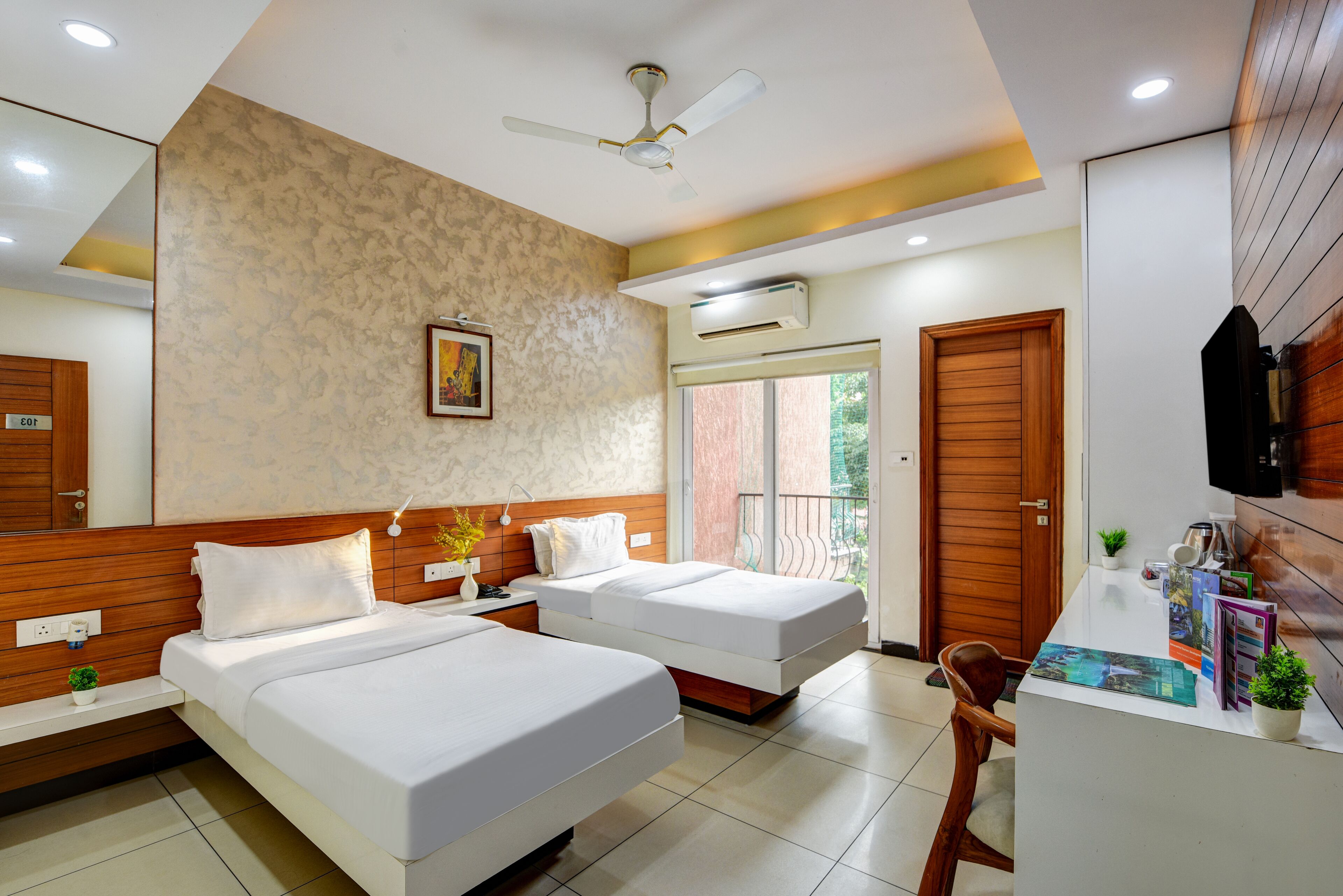A hotel room with two beds, a desk, a chair, a ceiling fan, and a large window.