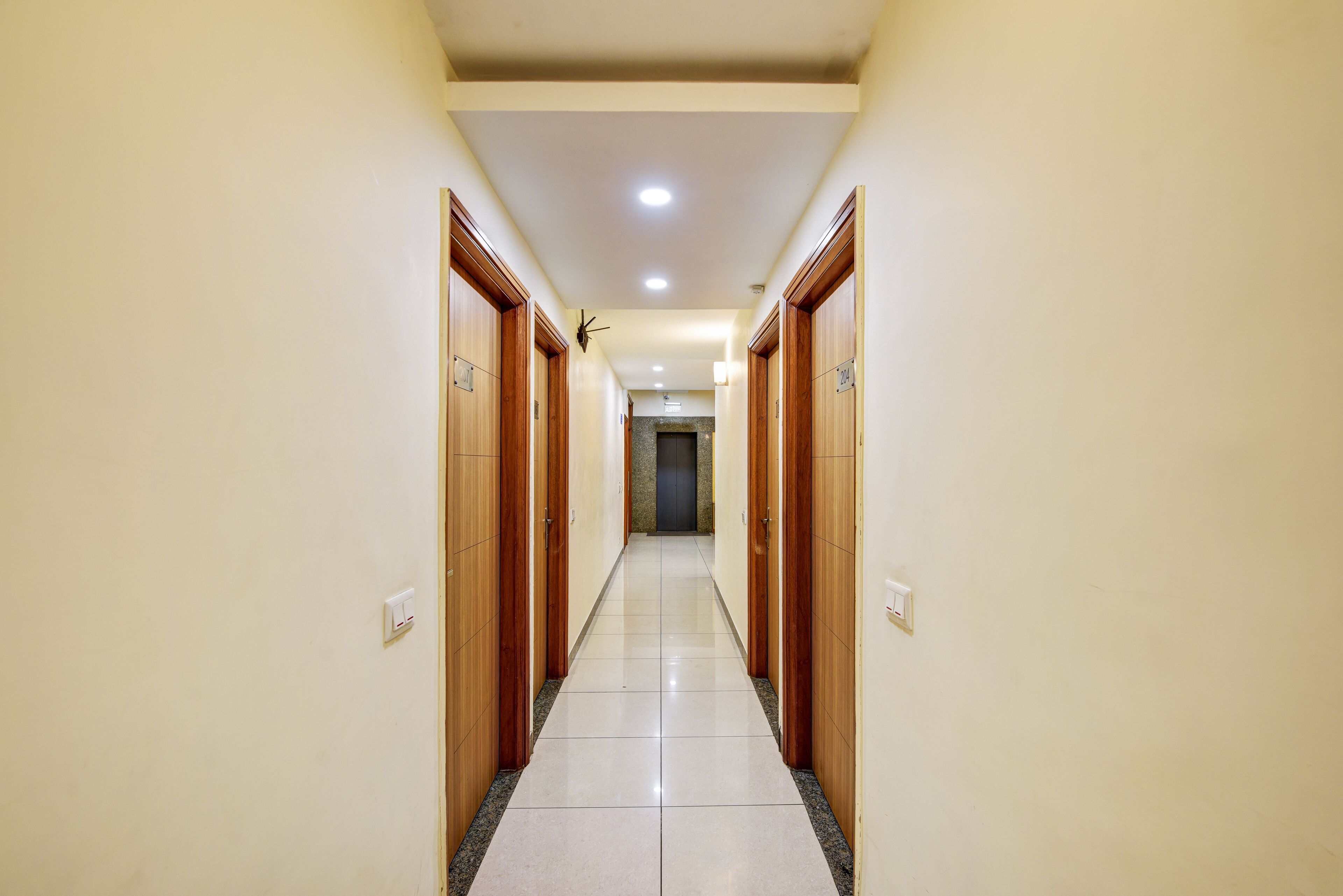 A hallway with wooden doors and a tiled floor, leading to a dark door at the end.