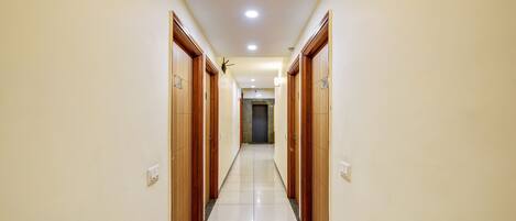 A hallway with wooden doors and a tiled floor, leading to a dark door at the end.