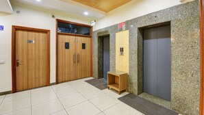 Un vest íbulo de hotel con puertas de madera, un mostrador de recepción y dos ascensores.