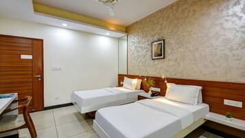 A hotel room with two single beds, a wooden desk, a chair, and a ceiling fan.