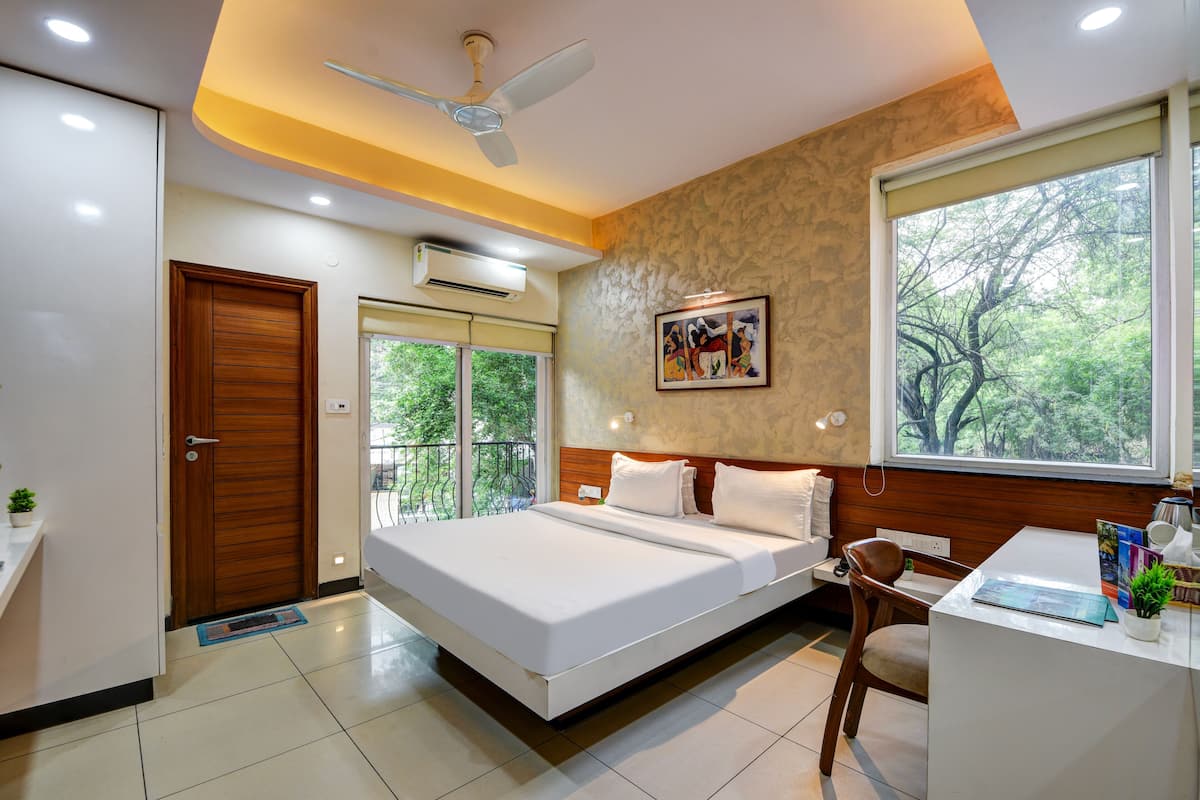 A modern hotel room with a bed, desk, and chair, a ceiling fan, and a large window with a view of trees.