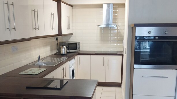 Una cocina moderna con armarios blancos, una isla de madera, microondas integrado y horno de acero inoxidable.