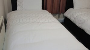 Una habitación de hotel con dos camas individuales, cada una con cabecero negro y ropa de cama blanca.