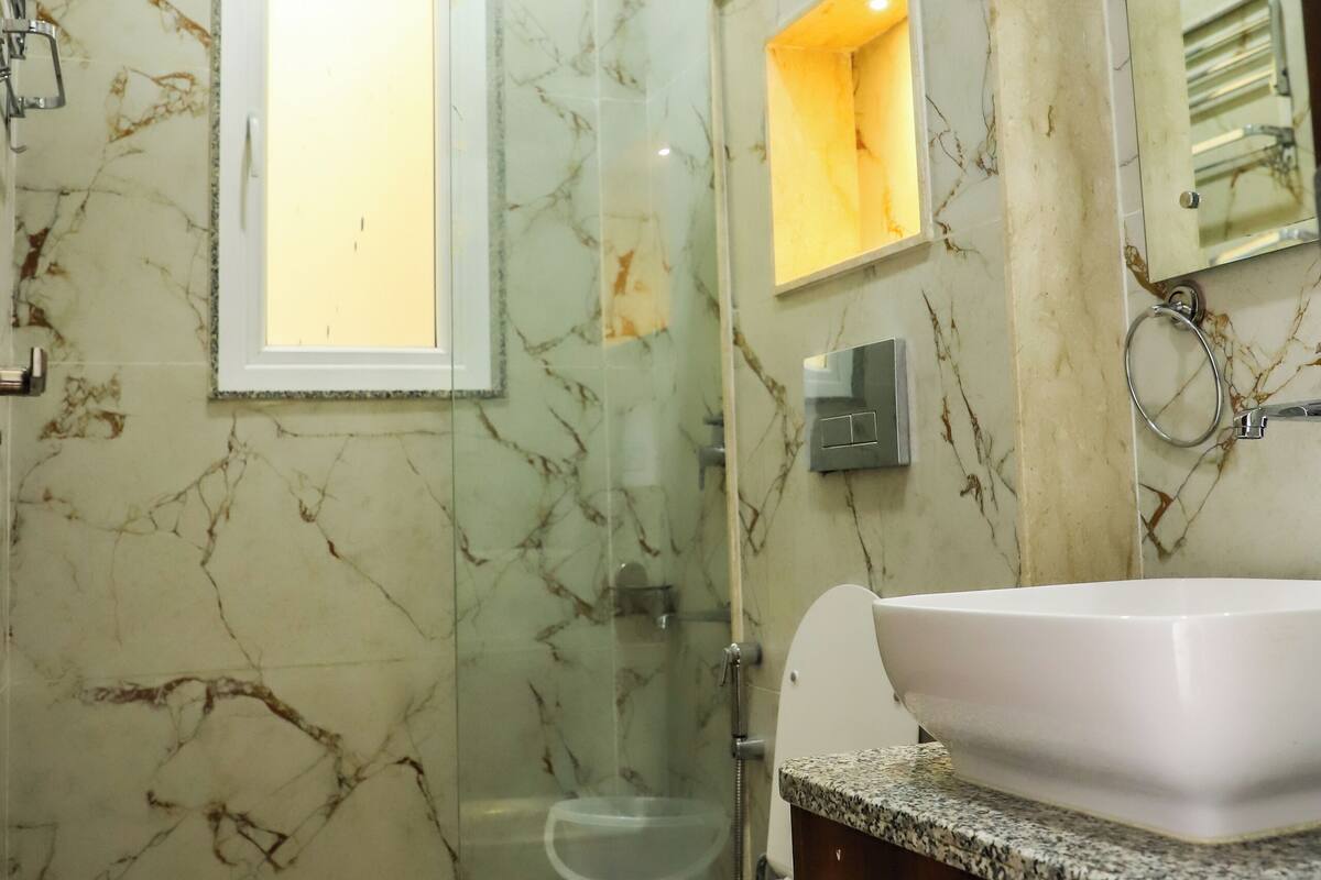 A bathroom with a marble wall, a glass shower enclosure, a white sink, and a toilet.