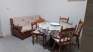 A dining area with a round table, floral tablecloth, wooden chairs, and a sofa with a floral pattern.