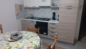 A small kitchen with a gas stove, a microwave, and a sink. There is a dining table with chairs and a floral tablecloth.