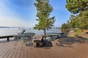 A wooden deck with outdoor seating, overlooking a calm lake with a pier extending into the water. - Cozy Pine Cove Cottage #5 (Tahoe Vista)