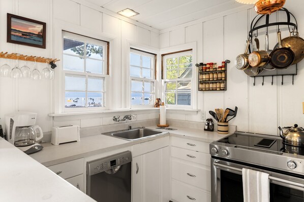 A kitchen with white cabinetry, a dishwasher, a stove, and a window with a view of the sea. - Cozy Pine Cove Cottage #5 (Tahoe Vista)
