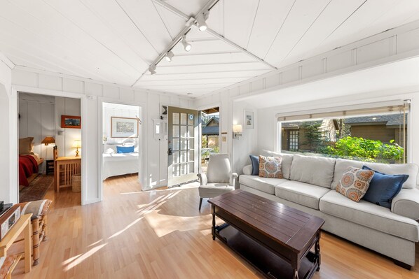 A spacious living room with a large window, a sofa, a coffee table, and a wooden floor.