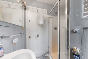A bathroom with a white sink, a mirror, a towel hanging on the door, and a shower area. - Cozy Pine Cove Cottage #5 (Tahoe Vista)