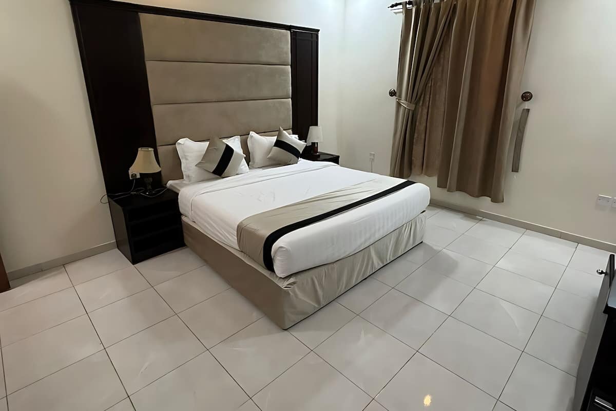 Una habitación de hotel moderna con una cama grande, una mesita de noche, una lámpara y una cortina.