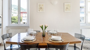 Een eetgedeelte met een houten tafel voor vier personen, omringd door stoelen. Boven de tafel hangen twee kunstwerken in lijsten.