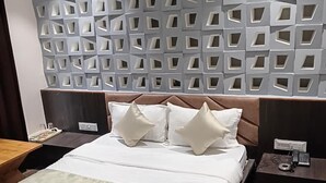 Una habitación de hotel moderna con una cama grande, un cabecero con recortes geométricos, una mesita de noche con un teléfono y otra mesita de noche con una lámpara.