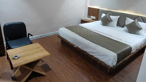 Una habitación de hotel con cama, mesita de noche, silla y un buró con lámpara.
